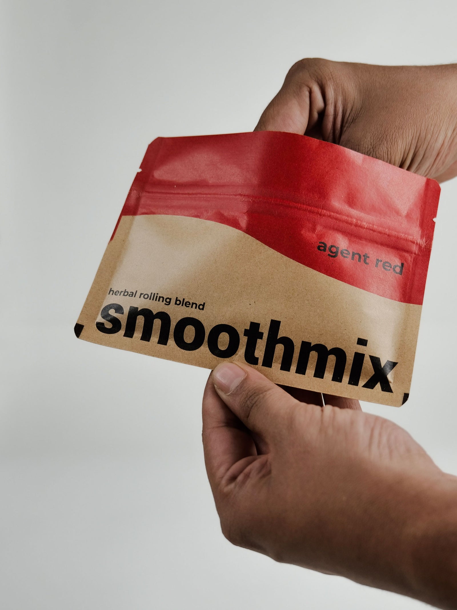 Hand holding a red and brown package of Smoothmix Agent Red herbal blend pouch 