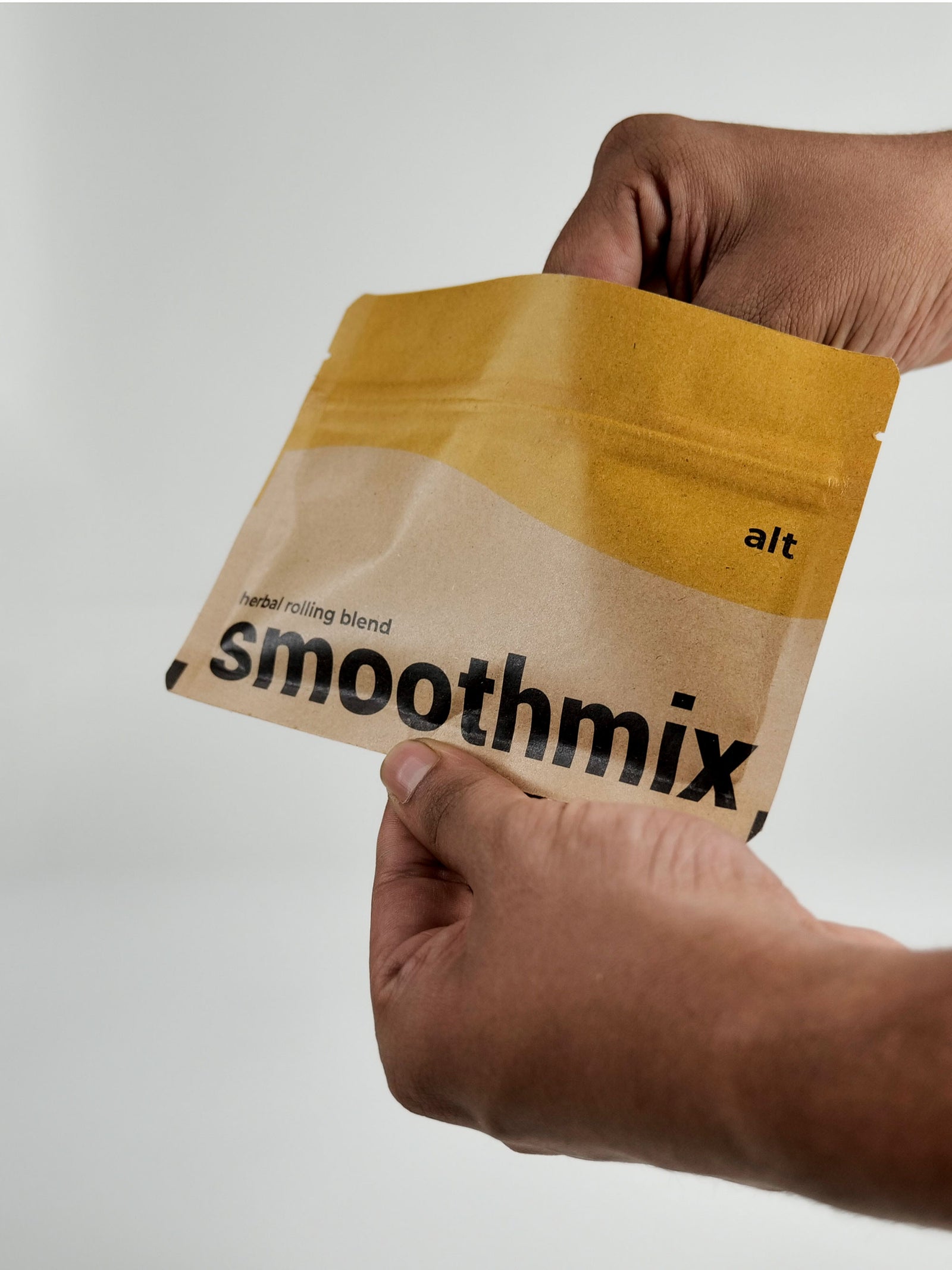 Hand holding a Smoothmix ALT tobacco-free herbal smoking blend package against a light gray background