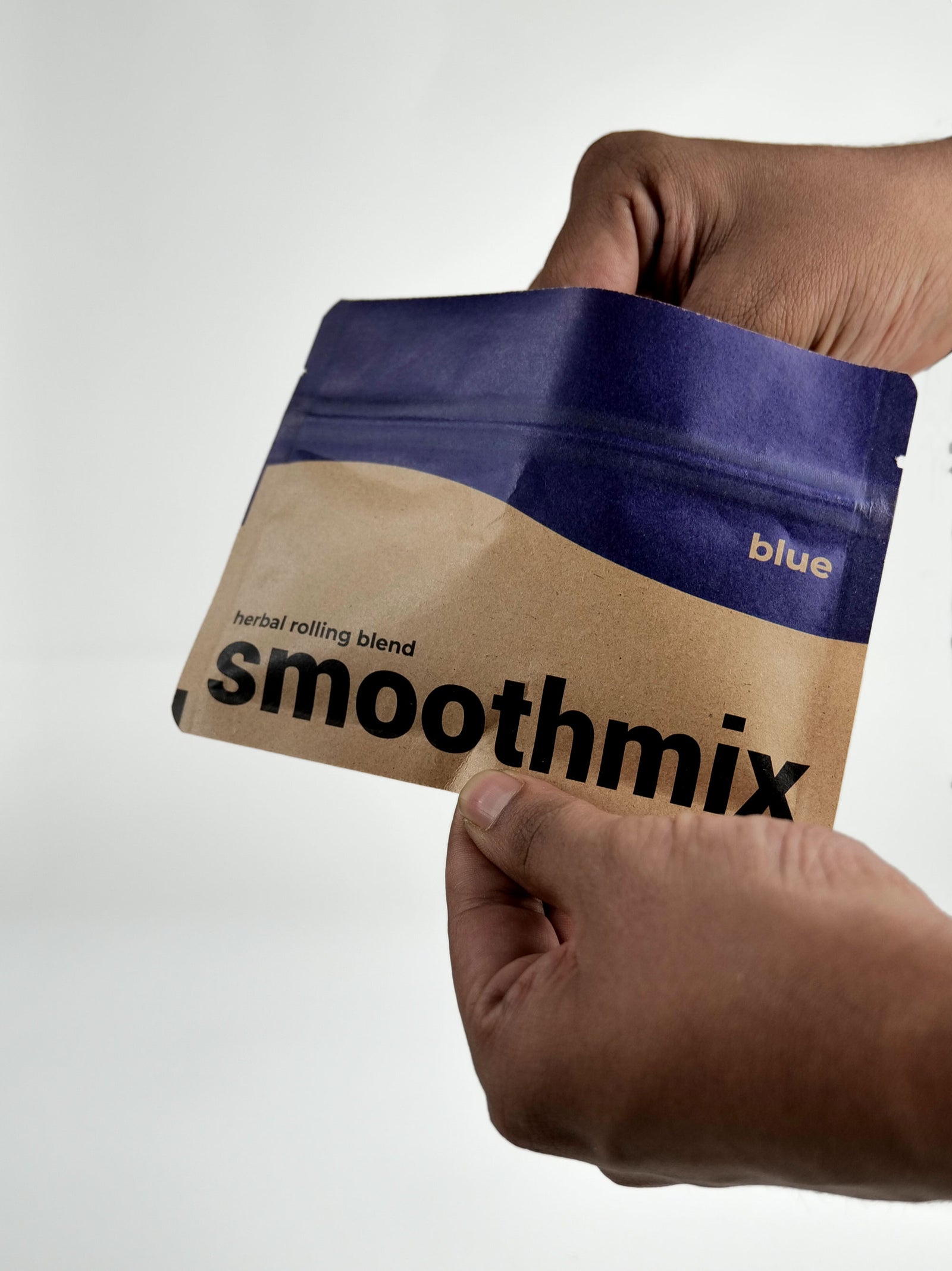 Hand holding a Smoothmix Blue herbal smoking package with blue and brown design on a white background