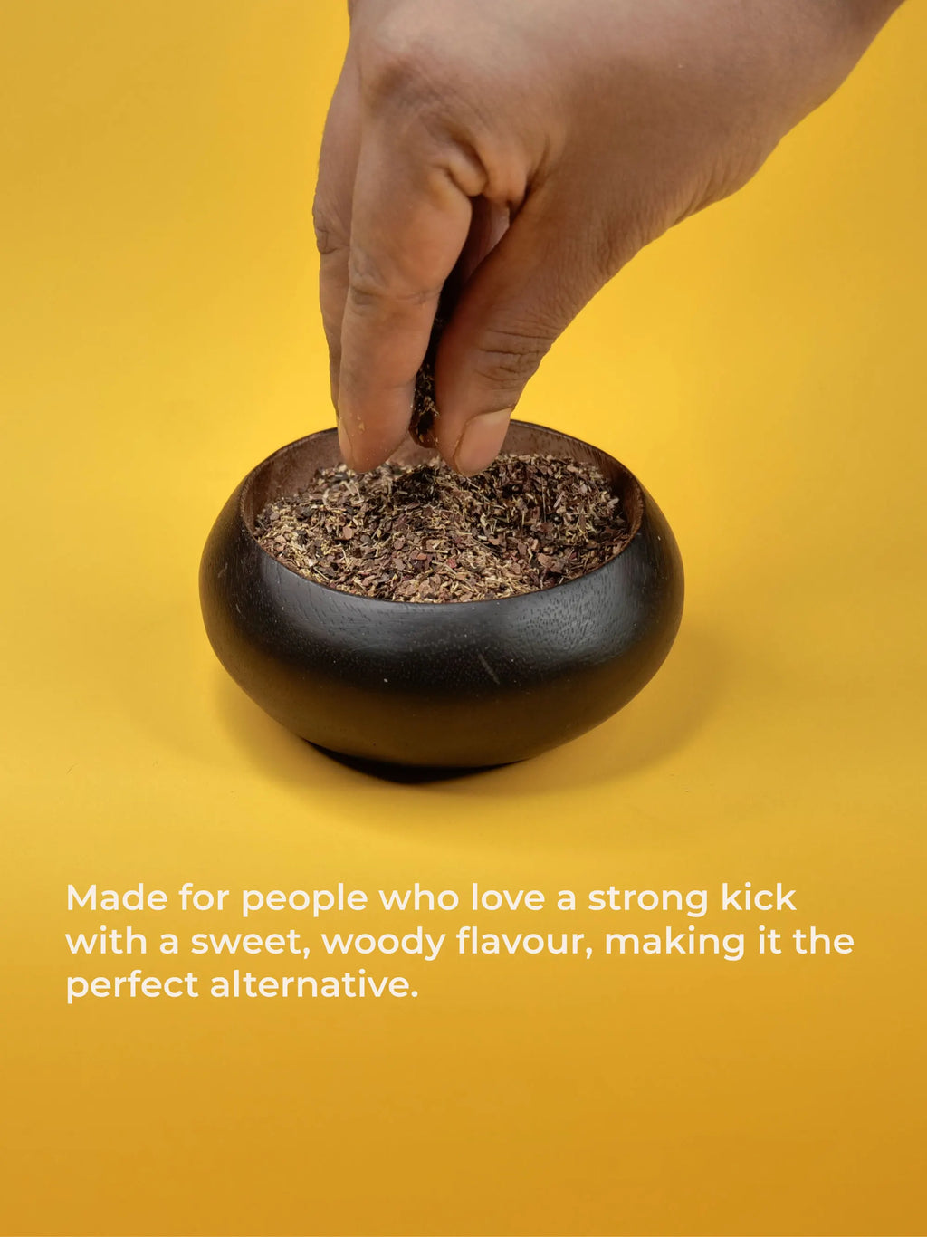Hand placing a small container of ground material into a black pot on a yellow background.