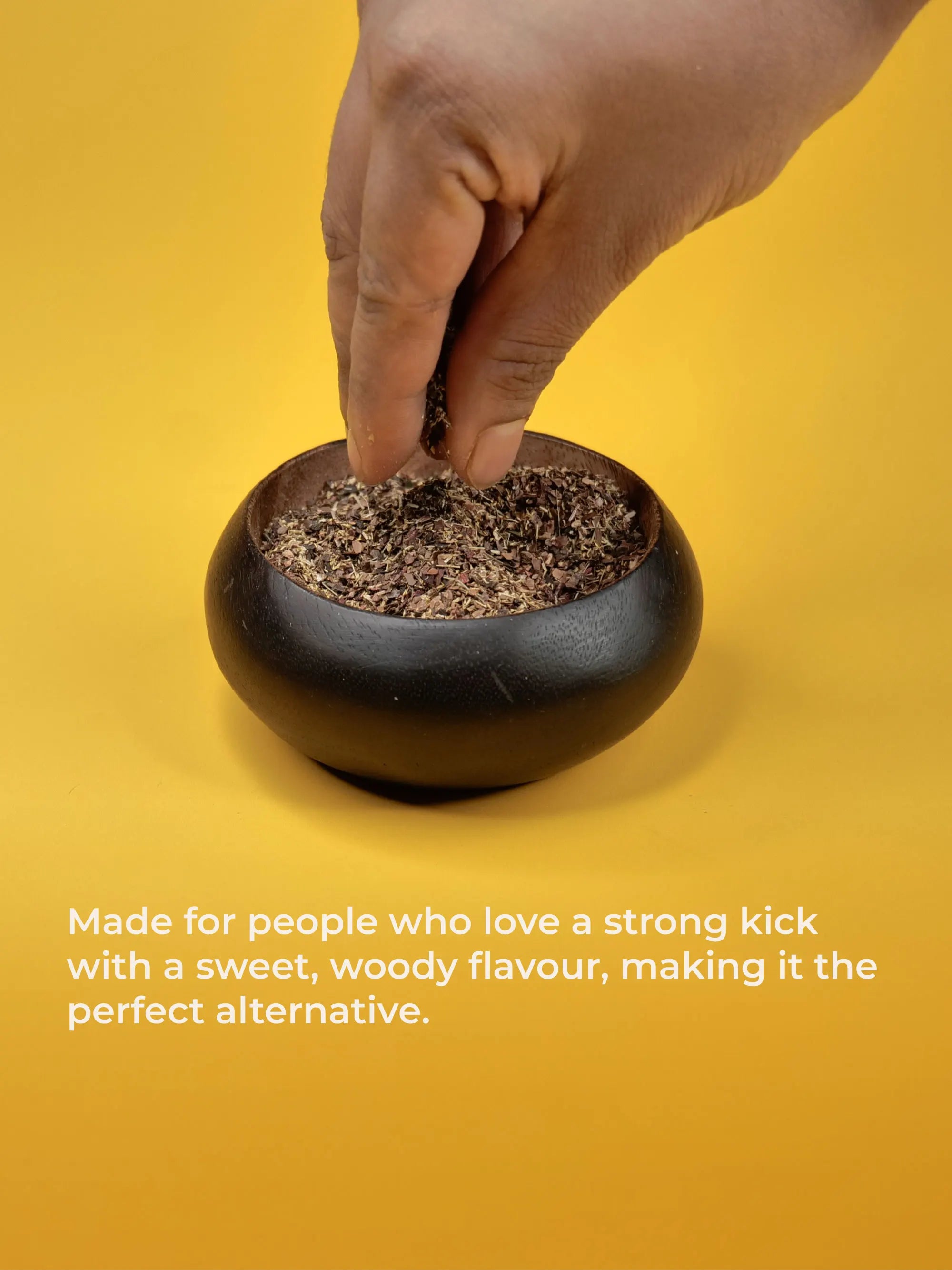 Hand placing a small container of ground material into a black pot on a yellow background.