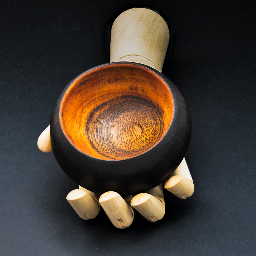 A uniquely handcrafted Smoothmix Cannabowl Mini bowl with a distinct grain pattern, featuring burnt edges and a black finish, held in a hand.